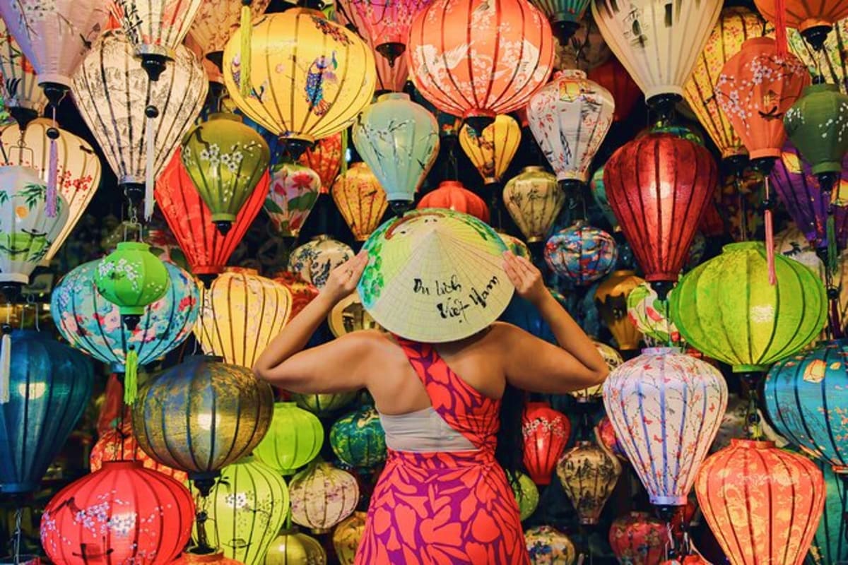 Woman holding a conical hat in front of colorful traditional Vietnamese silk lanterns hanging at Hoi An night market