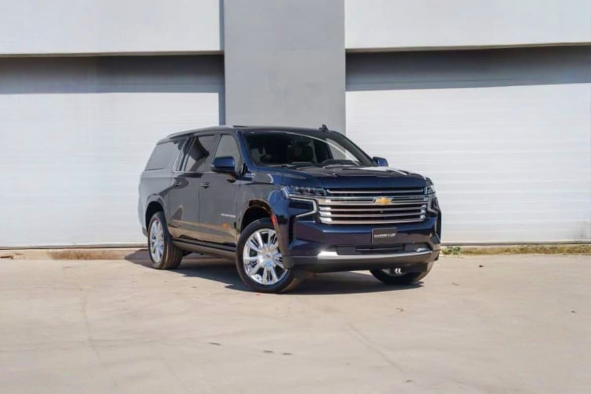 Dark blue Chevrolet Suburban SUV parked under concrete overpass on empty concrete surface during daytime