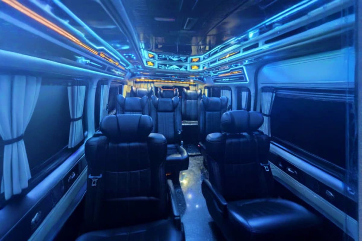 Interior of luxury coach bus with black leather seats, blue ambient lighting, and white curtains for airport transfer service