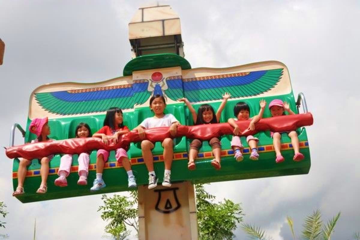 Children riding Egyptian-themed spinning amusement park ride at Legoland Malaysia with green wings and colorful decorations