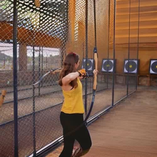 Hatta Wadi Activities Woman in yellow shirt drawing bow and arrow at outdoor archery range with targets