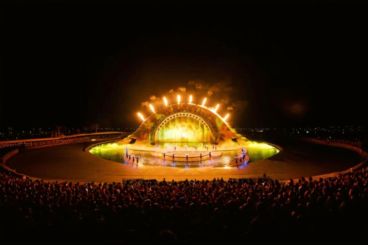 Kiss of the Sea Show Illuminated UFO-shaped stage structure with golden lighting and glowing lights around the dome at night, surrounded by large