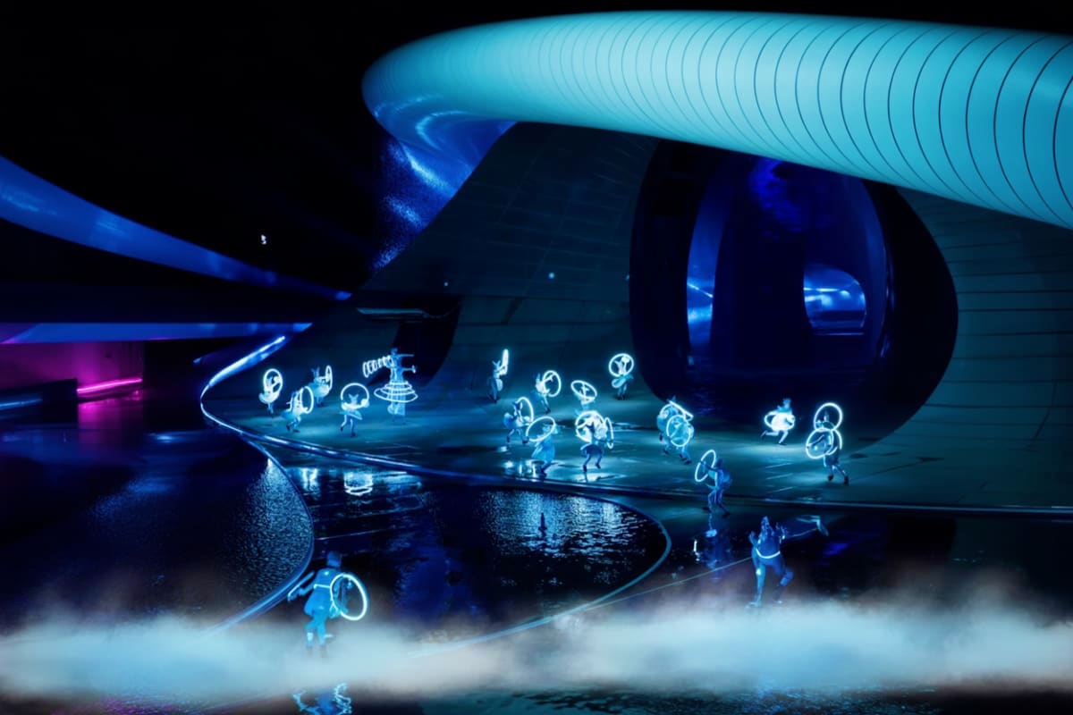 Kiss of the Sea Show Futuristic stage performance with glowing blue neon figures dancing on wet stage under large sculptural structures and dramat
