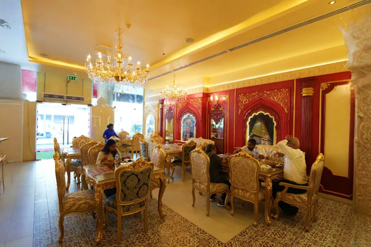 Luxurious dining hall at Mysore Palace Dubai with ornate gold chairs, crystal chandeliers, and red decorative wall panels wit