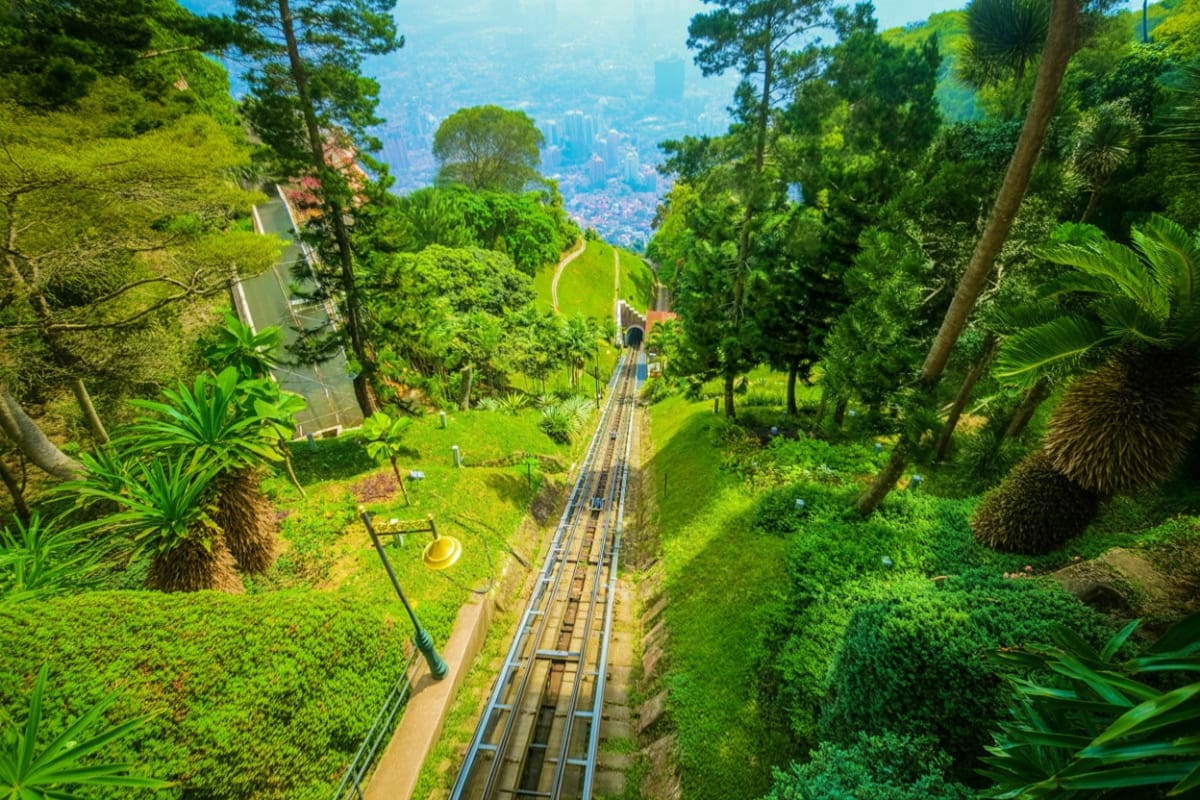 Aerial view of Penang Hill funicular railway tracks running through lush green forest with city skyline visible in the distan