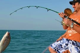 Deep Sea Fishing Abu Dhabi Man in orange shirt fishing from boat, bent rod with caught fish jumping in blue ocean water