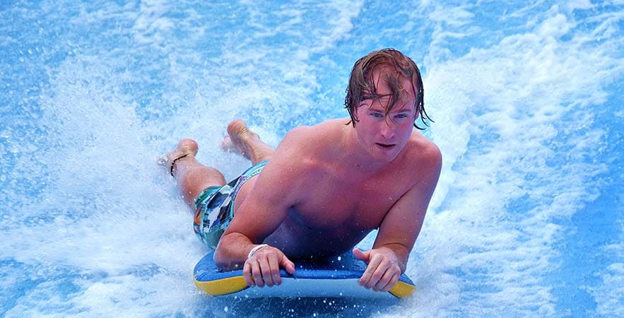 Full Day Sentosa Island Tour Young man bodysurfing on a blue wave at a water park or beach attraction on Sentosa Island