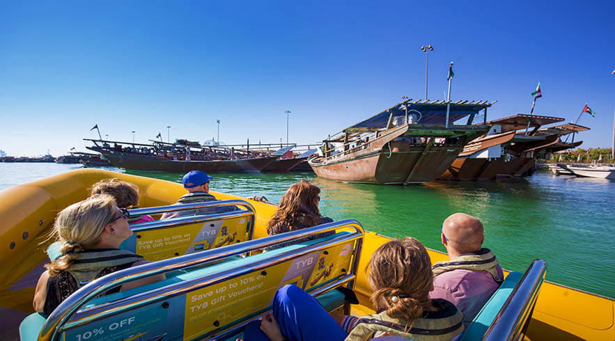 Tourists on a yellow speedboat tour viewing traditional wooden dhow vessels moored in Abu Dhabi's turquoise waters under clea
