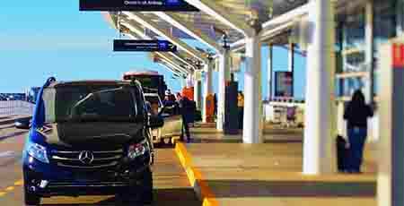 Black Mercedes vehicle at Dammam Airport covered parking area with passengers and airport terminal visible
