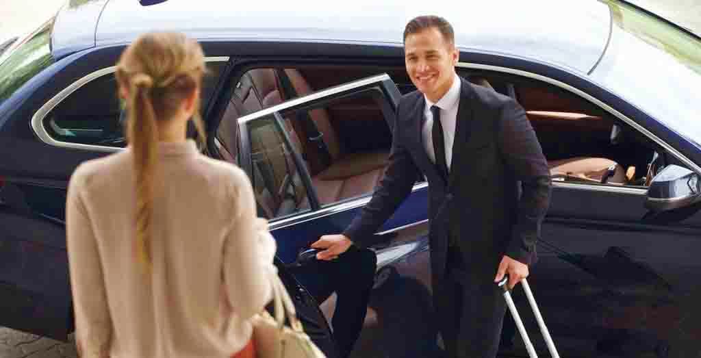 Professional chauffeur opening car door for passenger during intercity transfer service