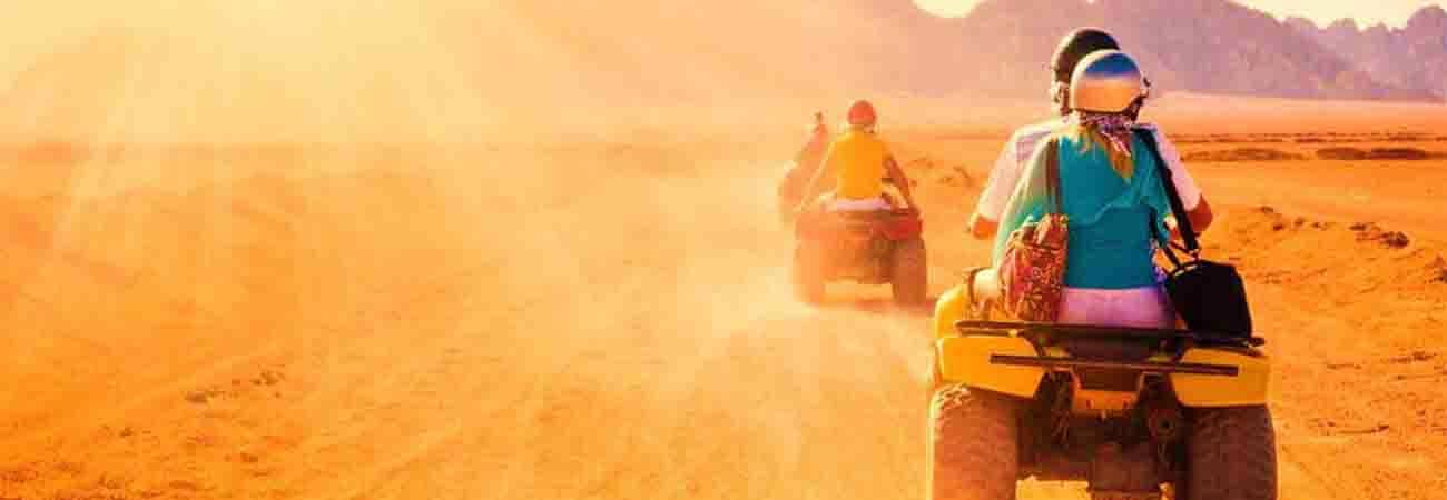 Tourists riding ATVs across sandy desert landscape with dust clouds in Jeddah, Saudi Arabia
