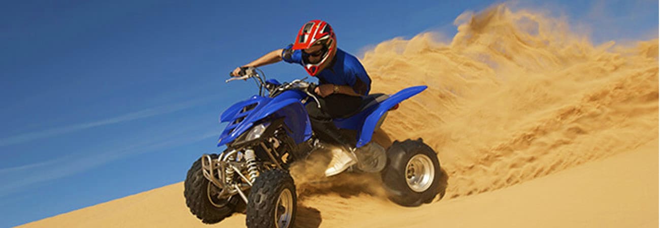 Person riding a blue ATV on sand dunes under clear sky during desert safari