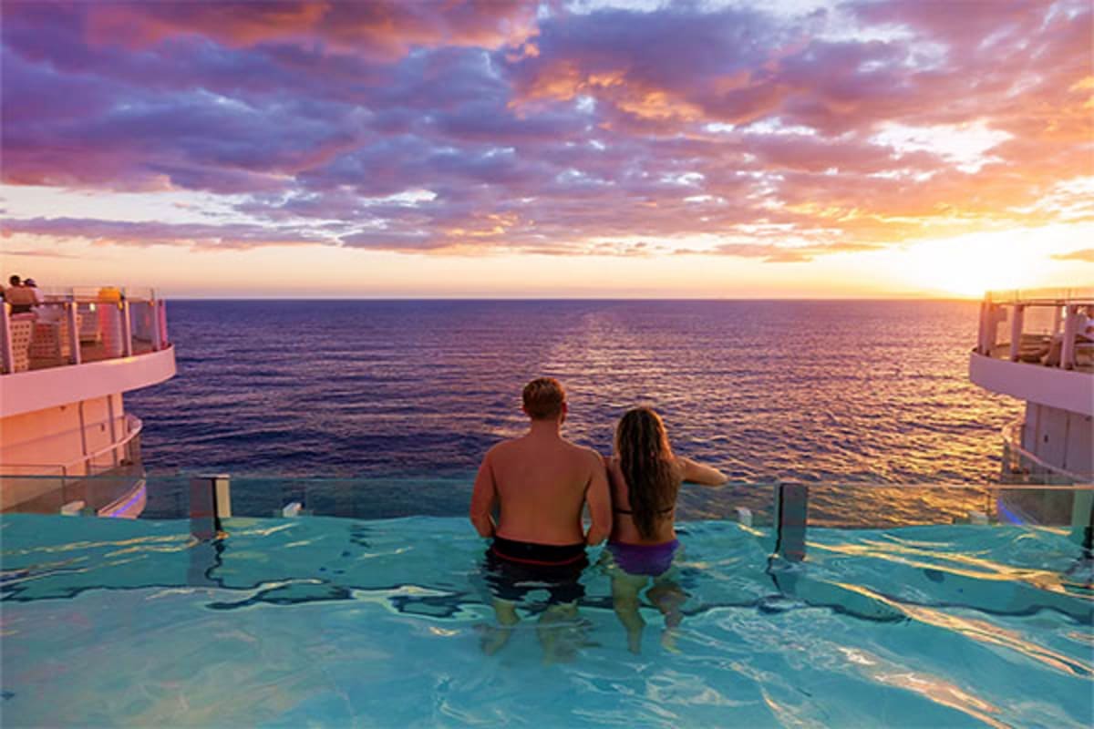 Couple relaxing in cruise ship pool at sunset overlooking the ocean with dramatic purple and golden sky