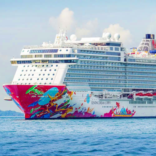 Large colorful cruise ship with pink and vibrant artwork on hull sailing on blue ocean water under cloudy sky
