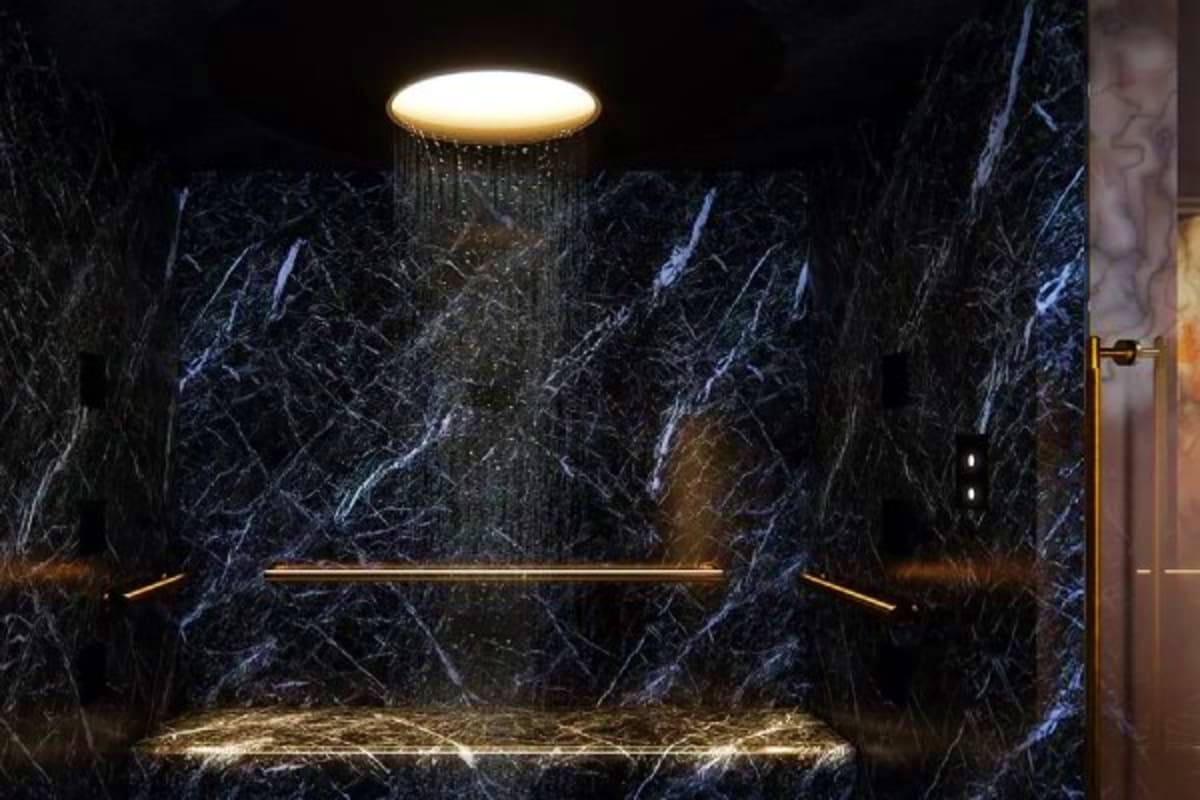 Norwegian Cruise Eastern Caribbean Cruise Luxury bathroom with black marble walls, gold fixtures, illuminated recessed ceiling light, and floating shelves in modern cr