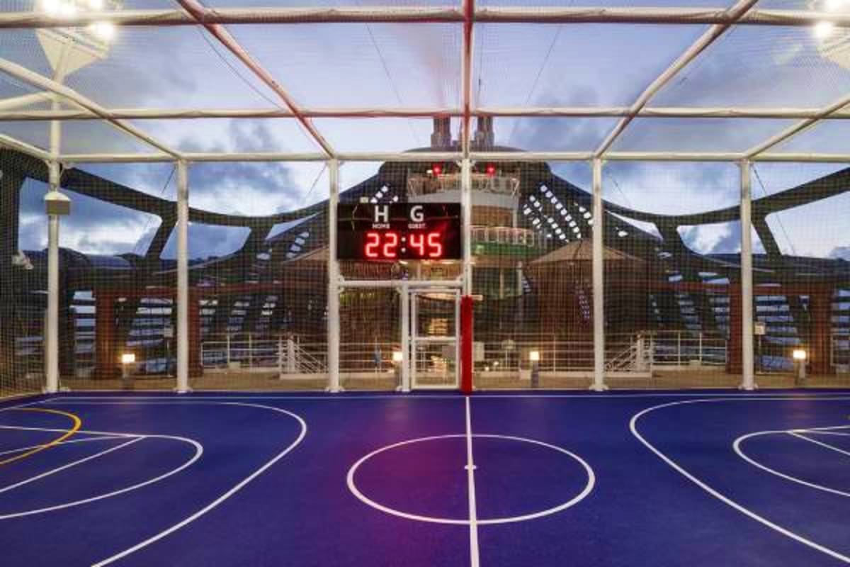 Indoor basketball court on MSC Fantasia cruise ship with digital scoreboard and glass ceiling showing sky and city skyline