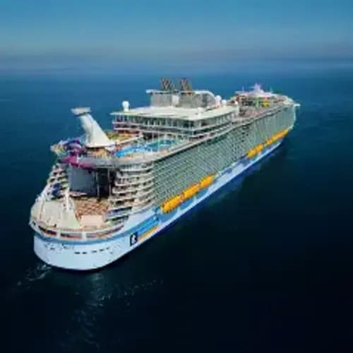 Aerial view of a large modern cruise ship on blue ocean waters with white superstructure and yellow hull stripe
