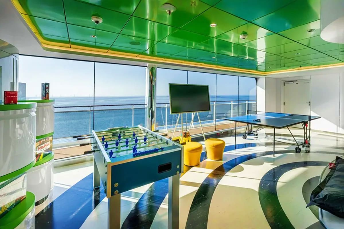 Modern cruise ship recreation deck with foosball table, ping-pong table, and ocean view through floor-to-ceiling windows unde