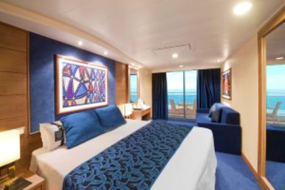 Luxurious cruise ship stateroom with ocean view, blue accent wall, queen bed, and balcony overlooking turquoise sea