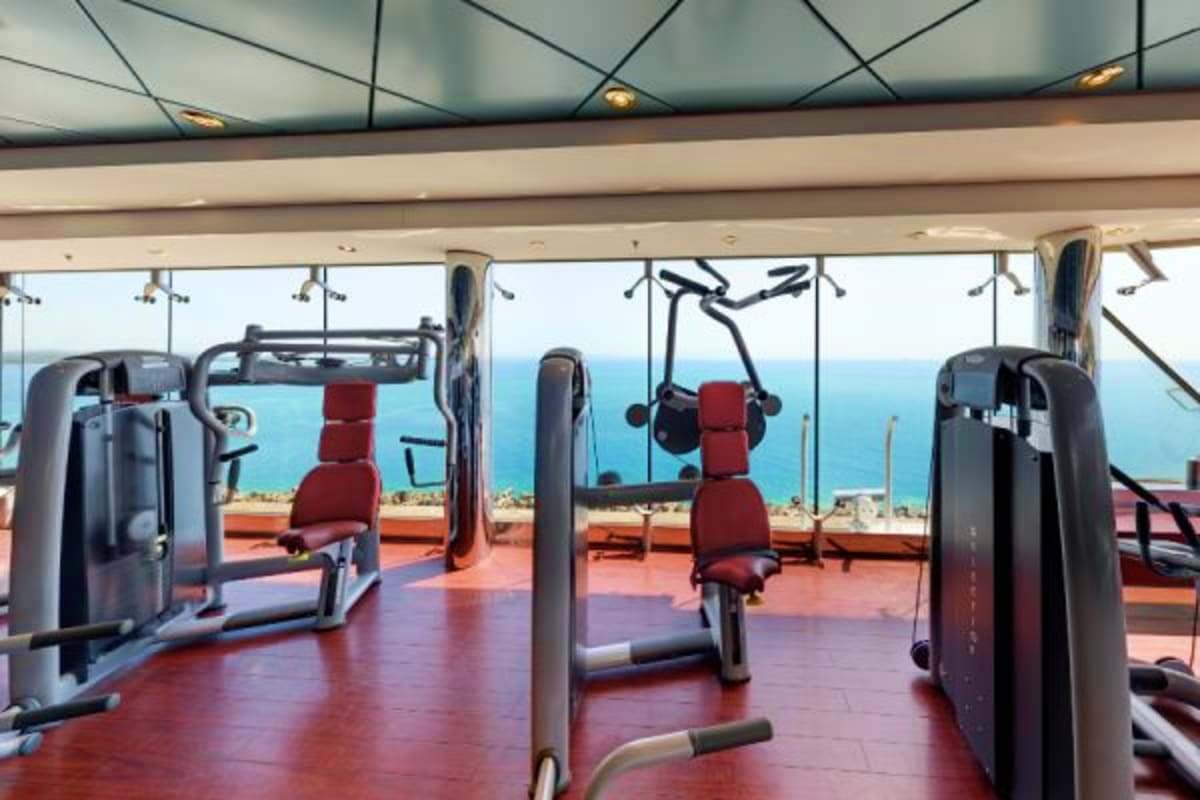 Modern gym with ocean and coastline views through floor-to-ceiling windows aboard MSC Magnifica cruise ship