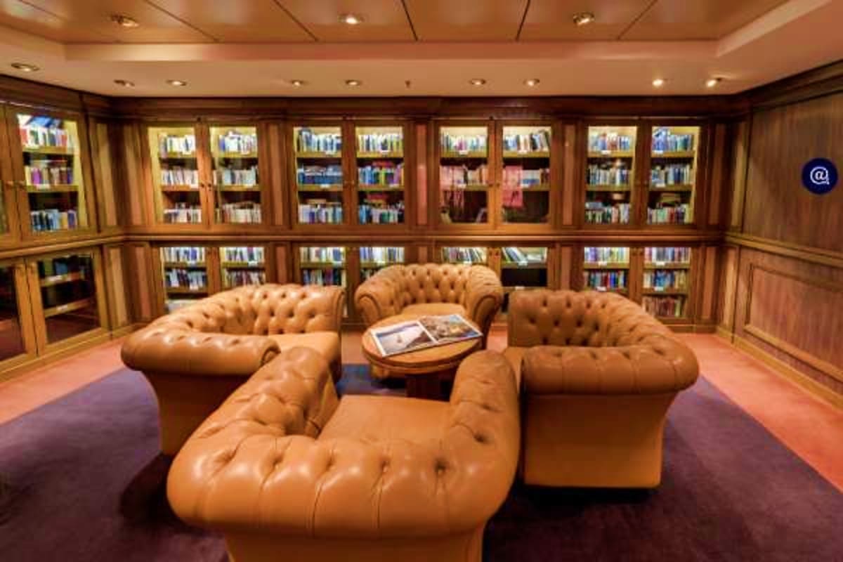 Luxury library lounge on MSC Magnifica cruise ship with tan leather Chesterfield seating, wooden book cabinets, and recessed 
