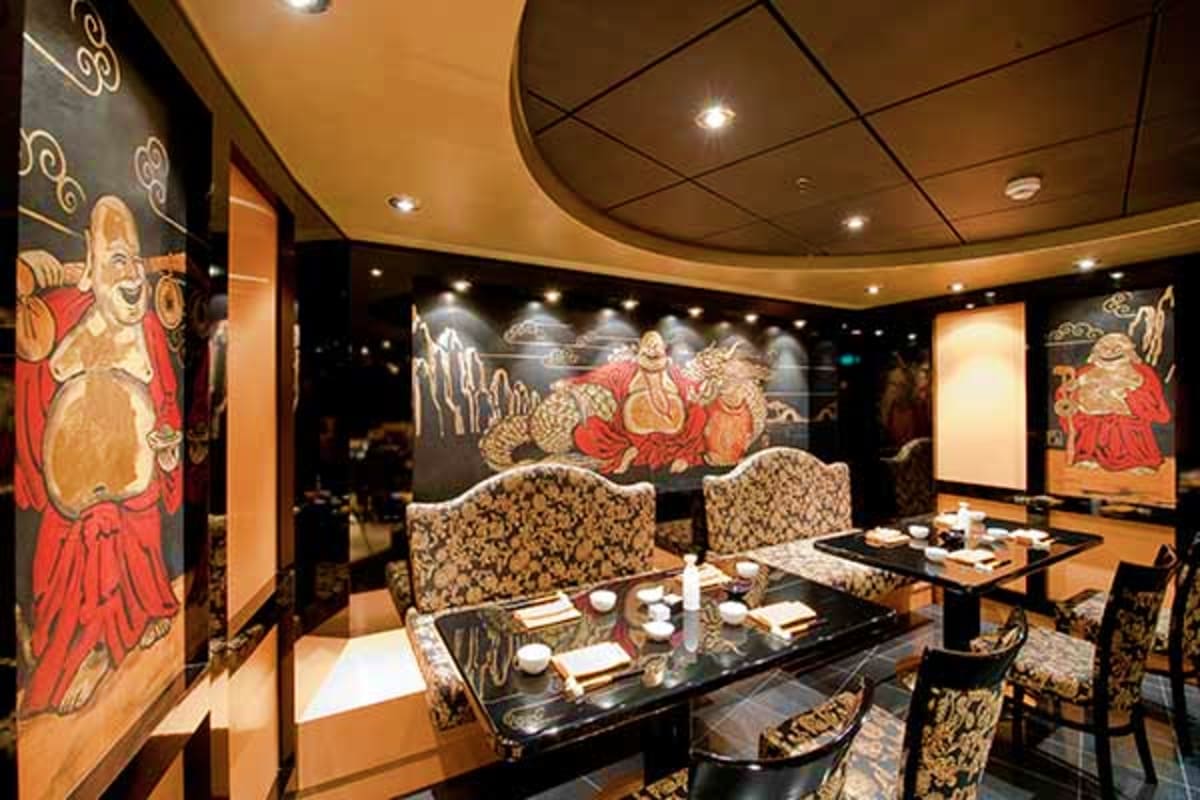 Upscale Asian fusion restaurant interior with ornate red and gold deity artwork on walls, black dining tables, and decorative