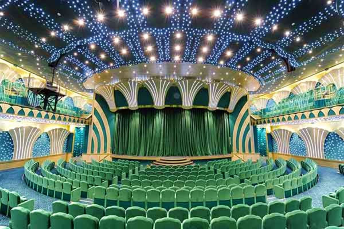 Ornate theater interior with green seats, decorative ceiling lights, and architectural arches typical of cruise ship entertai