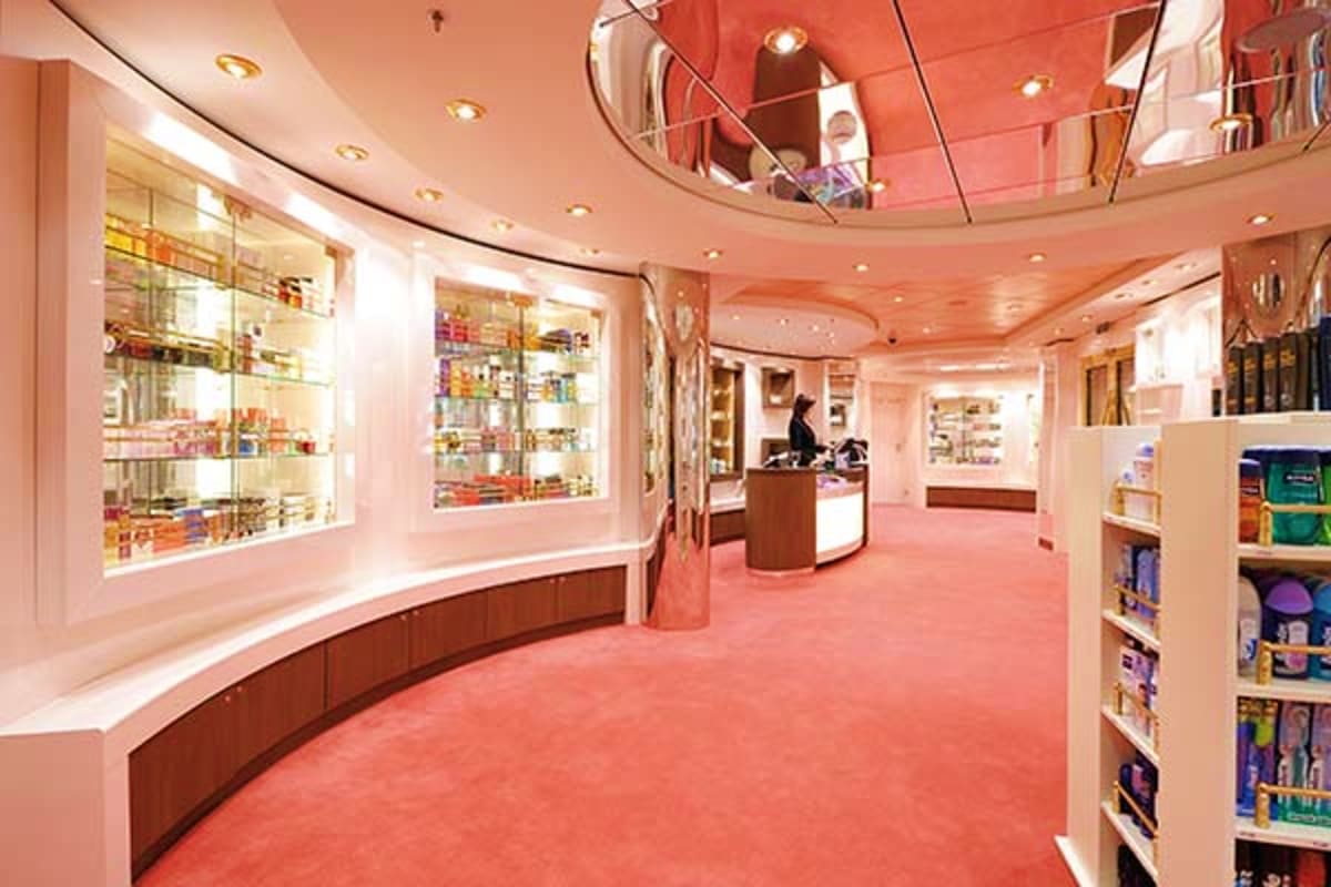 Modern cruise ship pharmacy interior with curved display cases, pink walls, recessed lighting, and product shelves