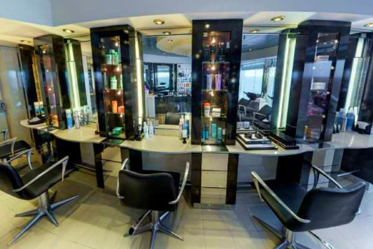 Modern hair salon with black and white styling stations, illuminated mirrors, and comfortable black chairs in a cruise ship i