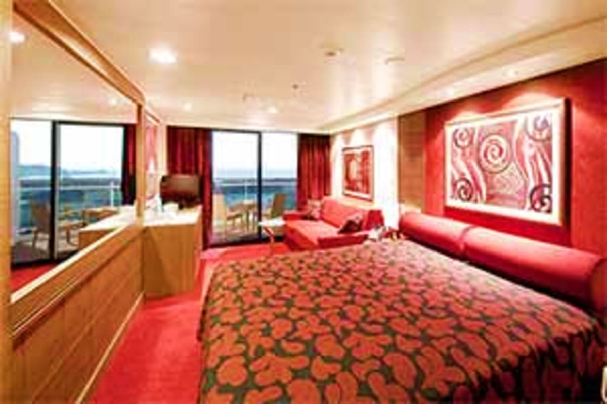 Luxury cruise ship suite with red decor, ocean view windows, bed, sofa seating, and modern lighting