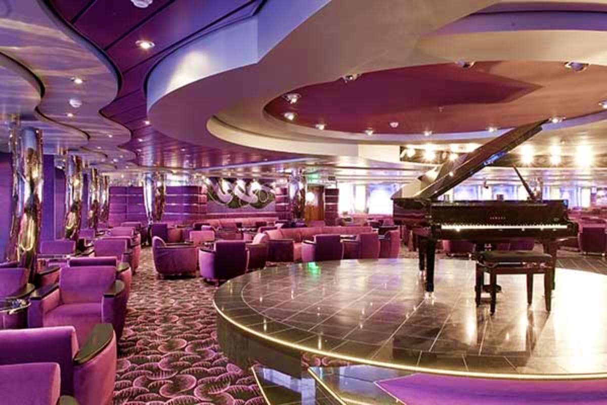 Luxury cruise ship theater lounge with grand piano, purple velvet seating, curved ceiling with ambient lighting, and polished