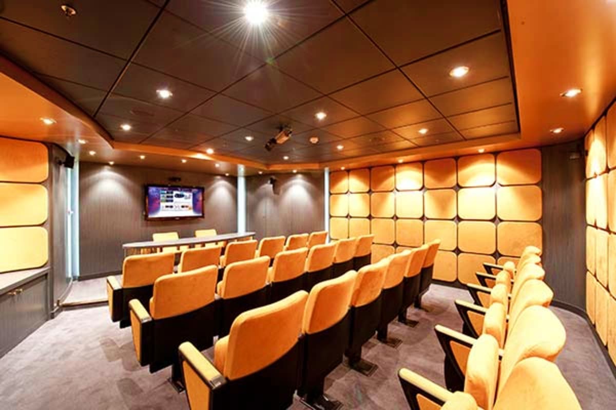 Modern home theater room with orange stadium seating, recessed lighting, and wall-mounted flat screen display