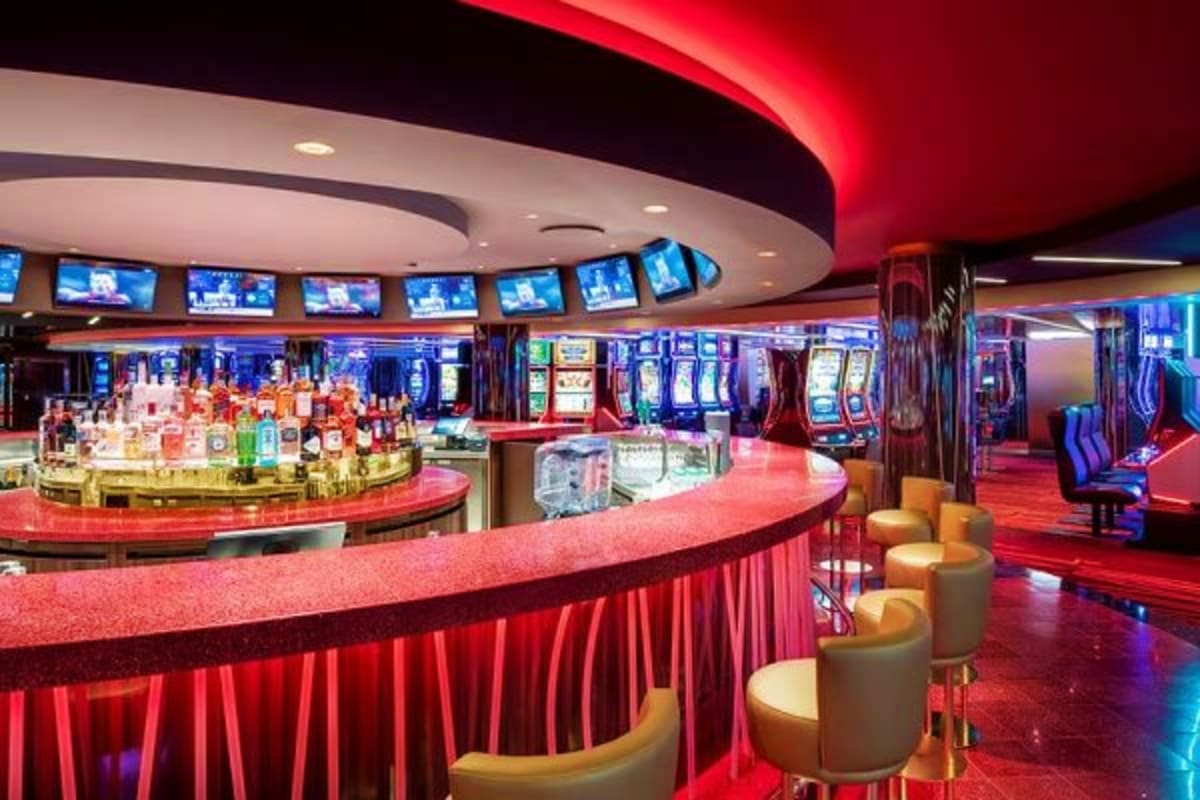Modern casino interior on MSC Euribia cruise ship with red ambient lighting, bar counter, slot machines, and curved ceiling d