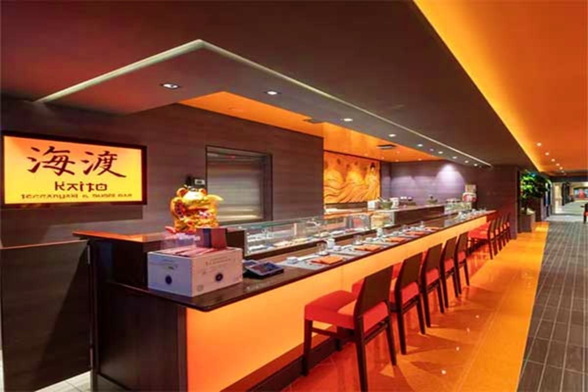 Modern sushi restaurant interior with orange and black design, chef counter, and red seating chairs along the service counter