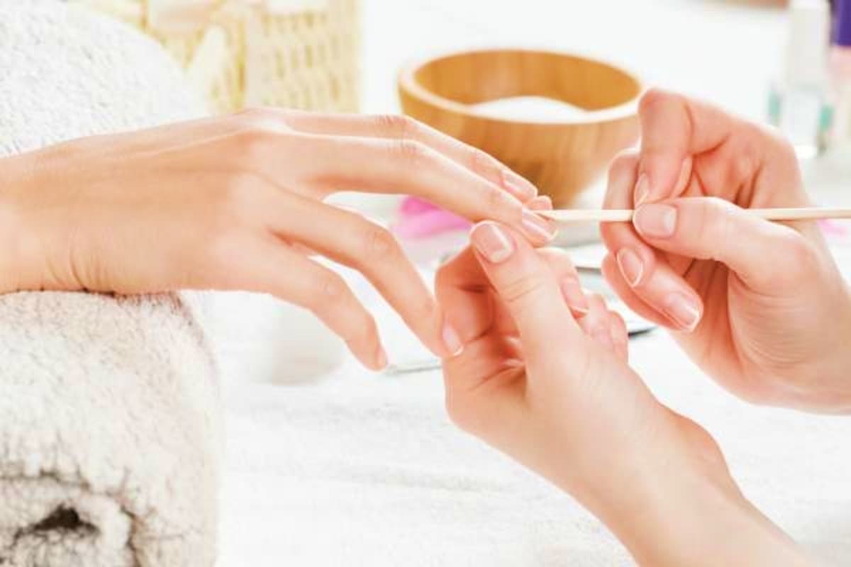 Manicurist applying pink nail polish to client's nails during spa treatment with wooden bowl in background