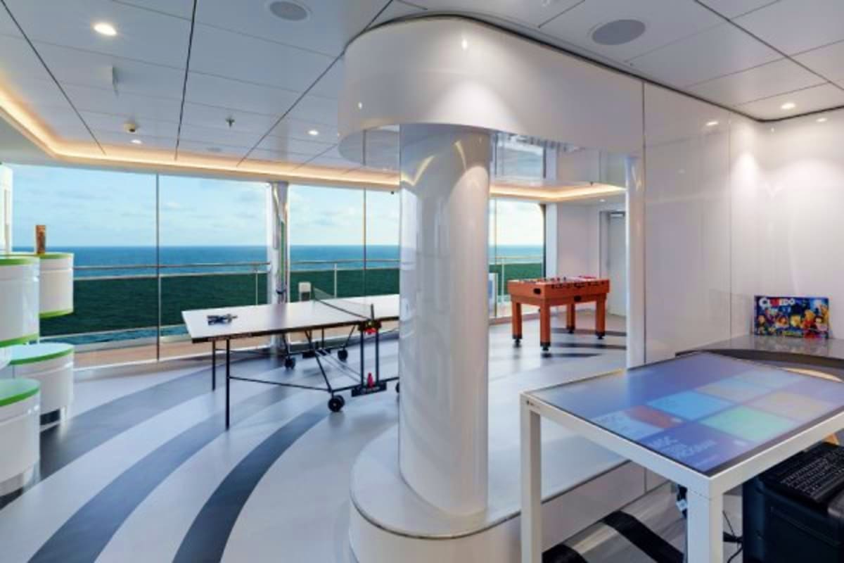 Modern cruise ship recreation room with ping pong table, foosball, and ocean views through floor-to-ceiling windows