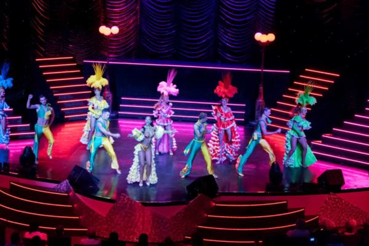 Colorful stage show performance with dancers in vibrant costumes under neon lighting and decorative backdrops on a cruise shi