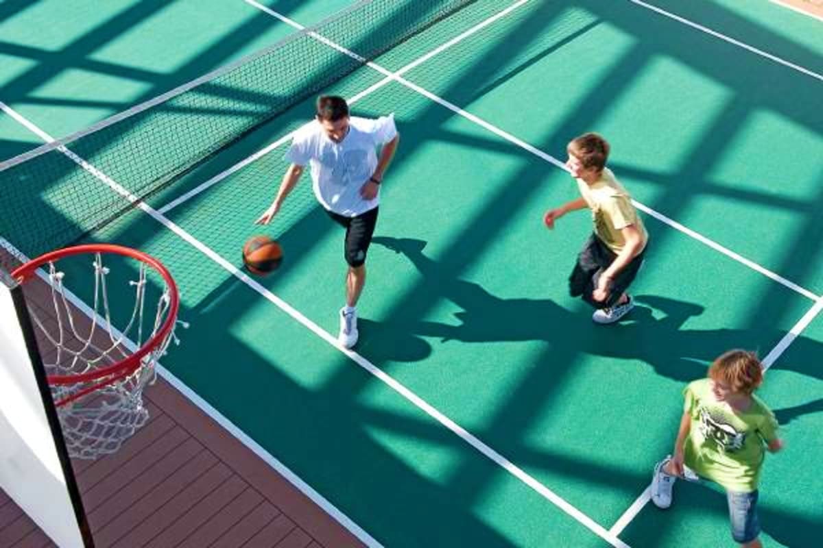 Overhead view of children playing basketball on a green outdoor court on a cruise ship, with a red hoop visible on the left s