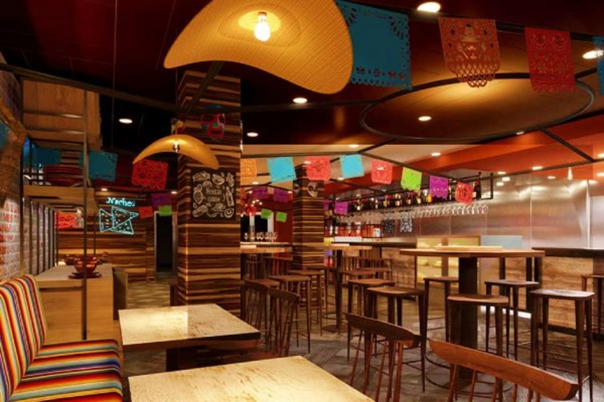 Modern Mexican restaurant interior with colorful papel picado decorations, wooden furnishings, bar counter, and warm ambient 