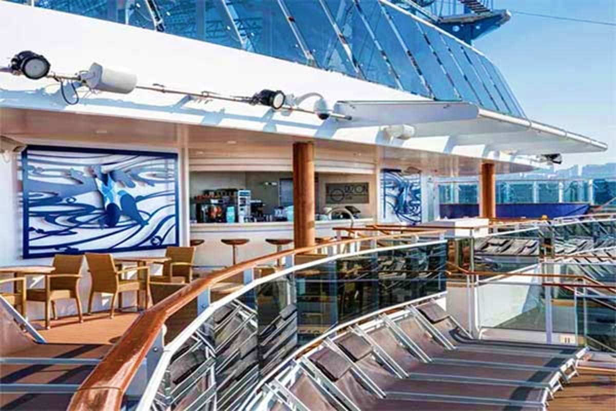 Cruise ship deck with lounge chairs, bar area with blue artwork, and retractable solar panel canopy overhead on MSC Euribia