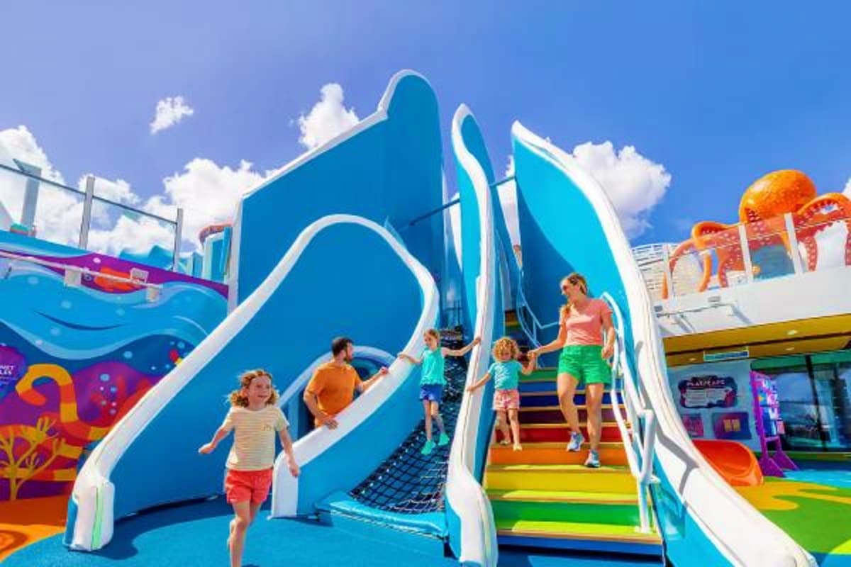 Children playing on colorful blue and white water slide at cruise ship waterpark on sunny day