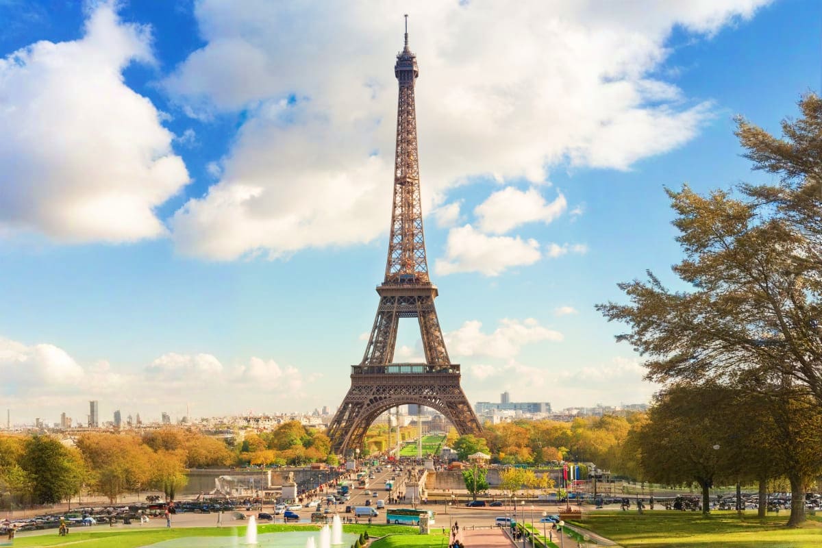 Eiffel Tower in Paris with Trocadéro Gardens, autumn trees, and Paris cityscape under blue sky with white clouds