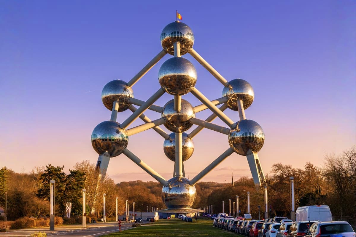 Atomium monument in Brussels with golden spheres and connecting tubes against purple sky, surrounded by parked cars