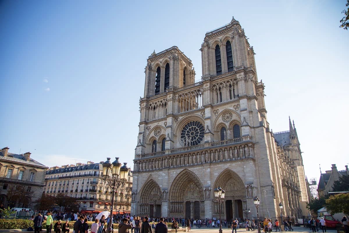 Notre-Dame Cathedral facade with twin towers and rose window in Paris, tourists gathered in front square