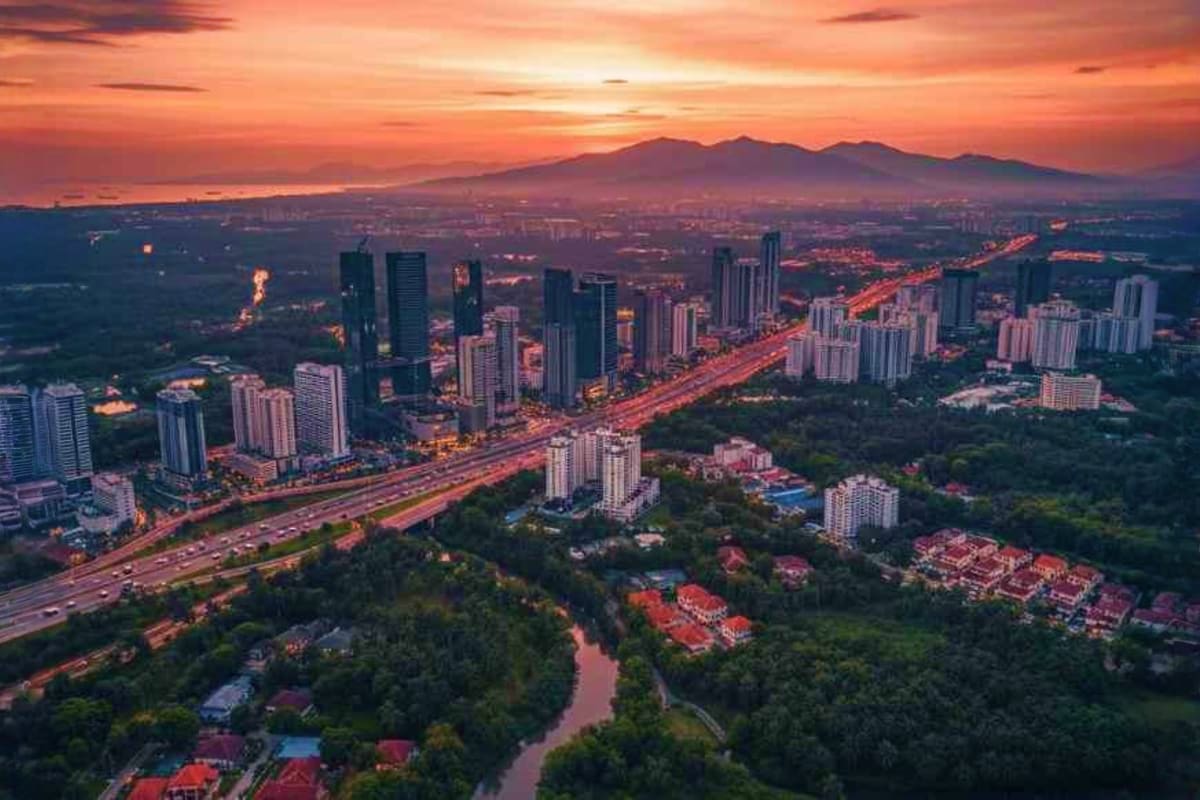 Aerial sunset view of modern city skyline with illuminated highway, residential towers, and mountain backdrop in Malaysia