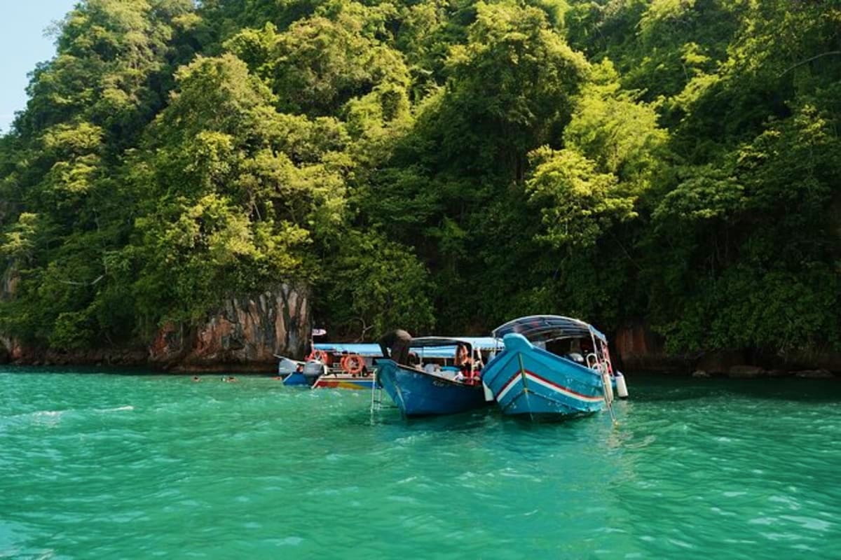 Blue longtail boats anchored in turquoise water with towering limestone cliffs and lush green forest in background