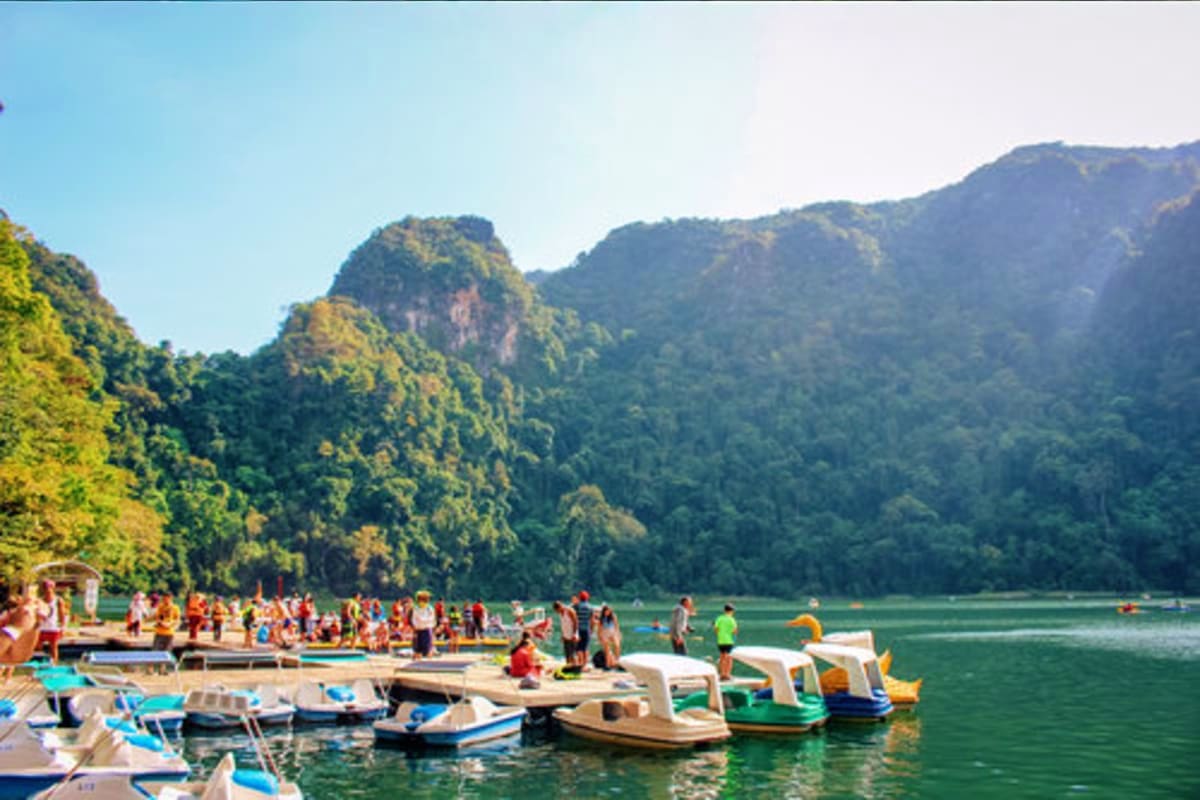 Tropical lake surrounded by lush green limestone cliffs with tourists and colorful boats at a beach pier in Malaysia
