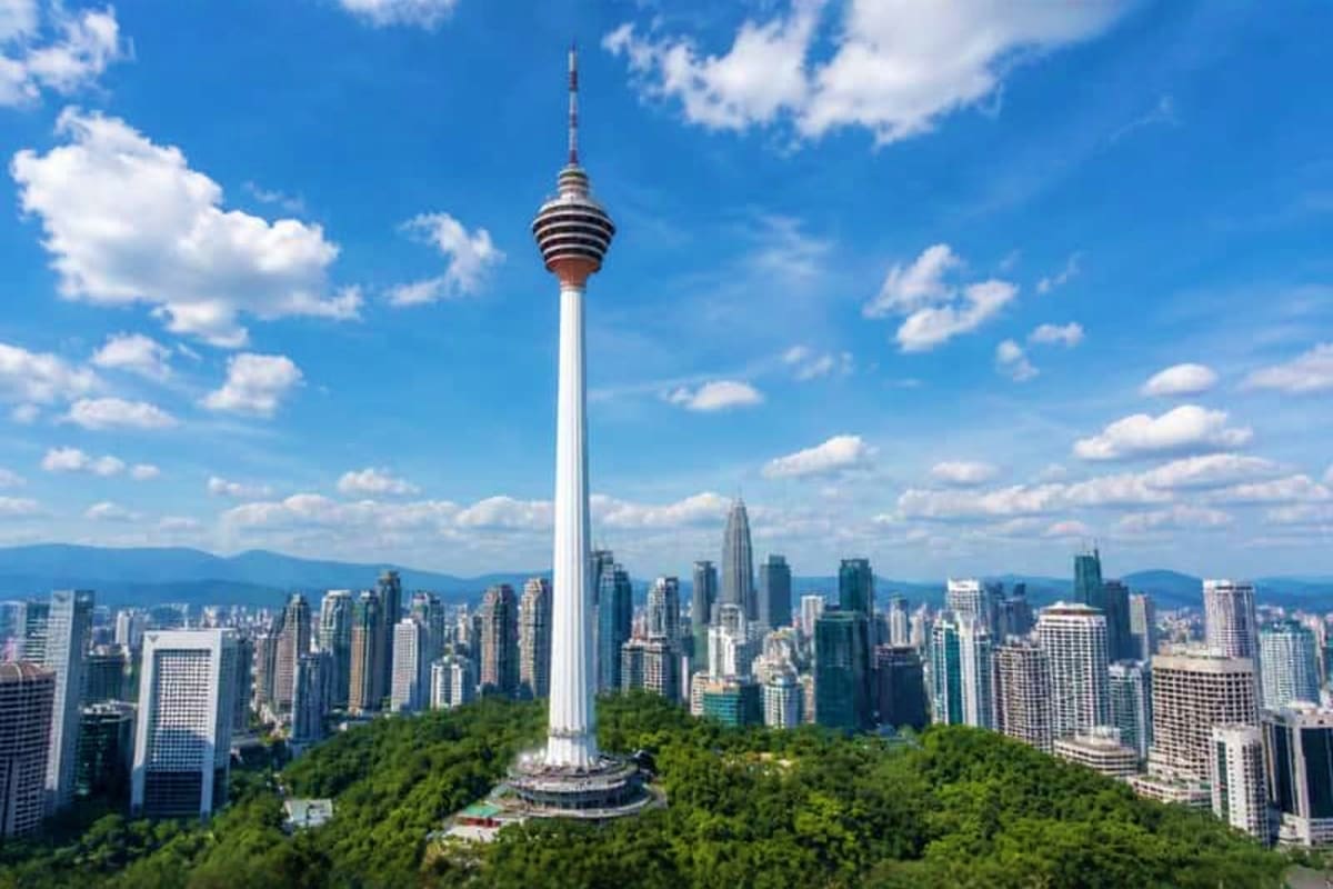 Menara Kuala Lumpur tower with city skyline and surrounding green forest against blue sky with white clouds