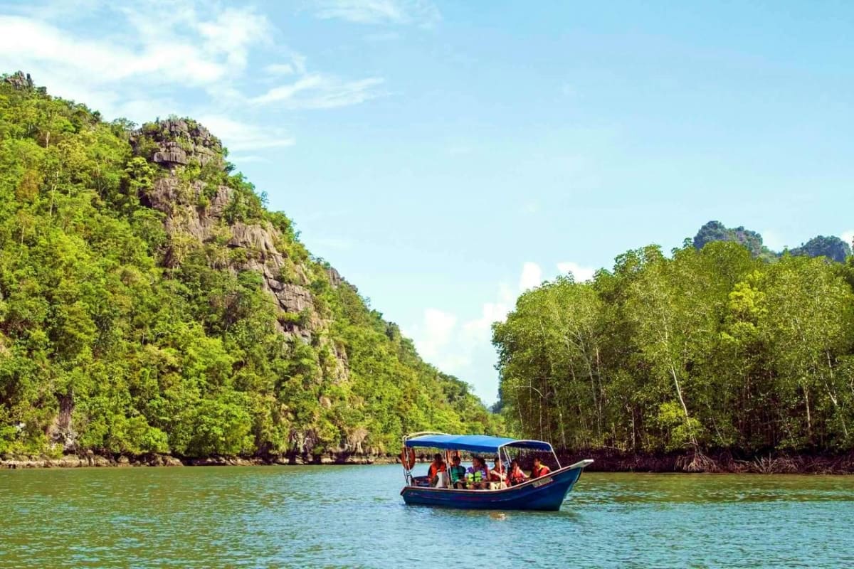 Traditional blue boat with tourists navigating turquoise waters surrounded by limestone cliffs and mangrove forests in Malays