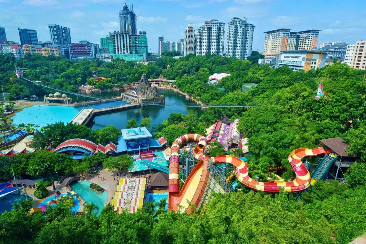 Aerial view of a theme park with colorful water slides, swimming pools, and a temple structure surrounded by lush green fores
